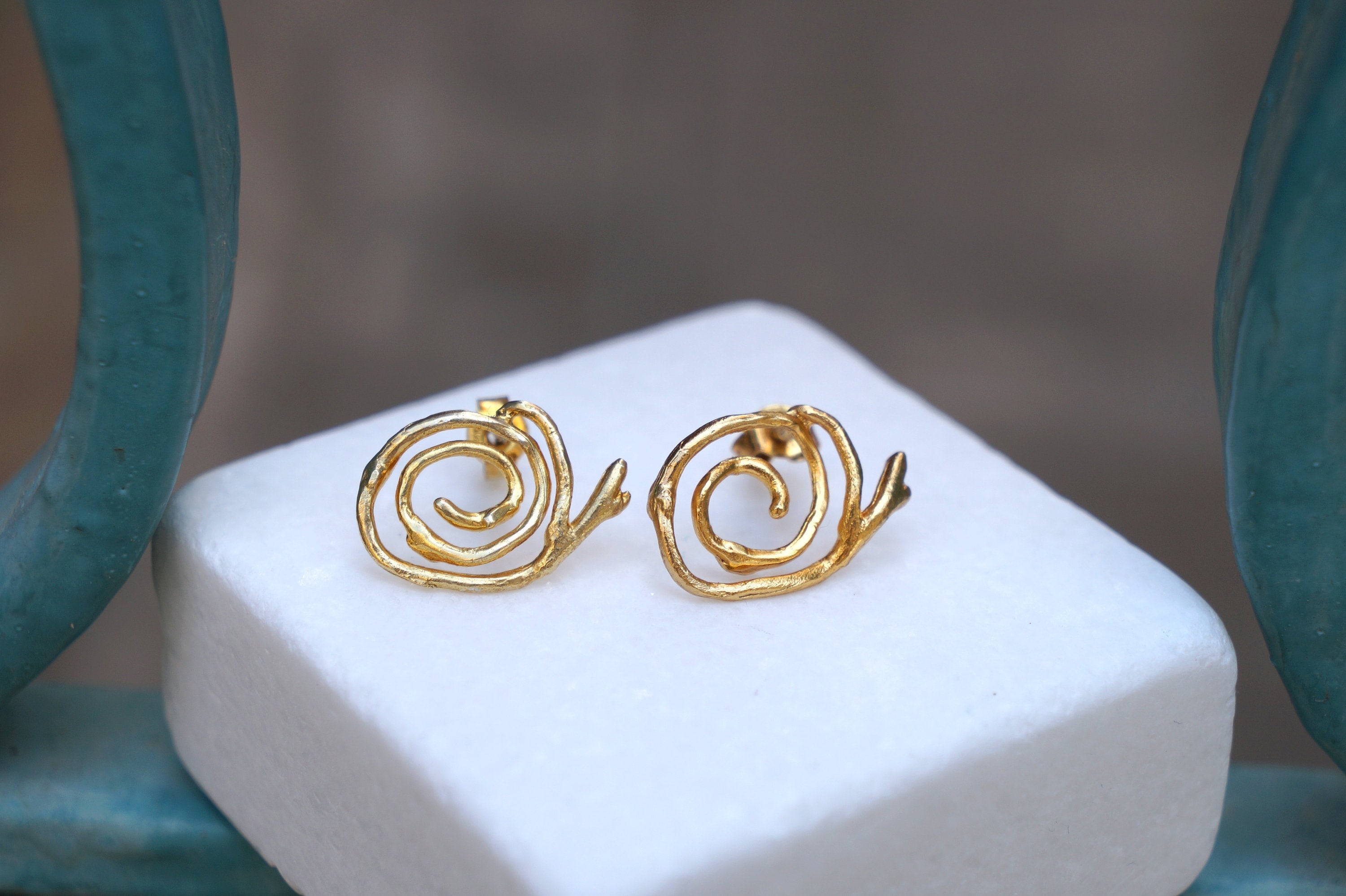 A pair of gold earrings with spiral designs, placed on a white surface.