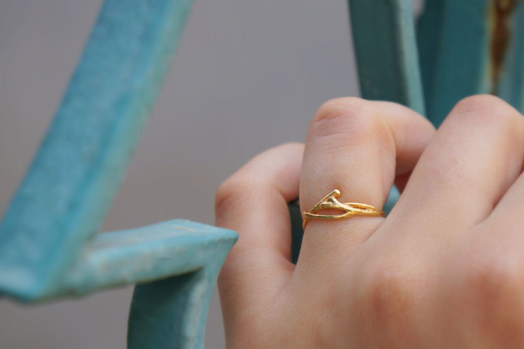 A close-up of a person's hand wearing a gold ring with a leaf design.