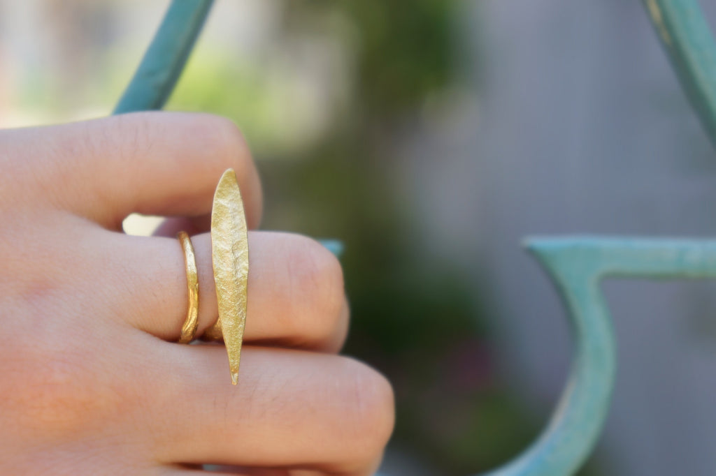 A close-up of a person's hand wearing a gold ring with a unique, elongated design.