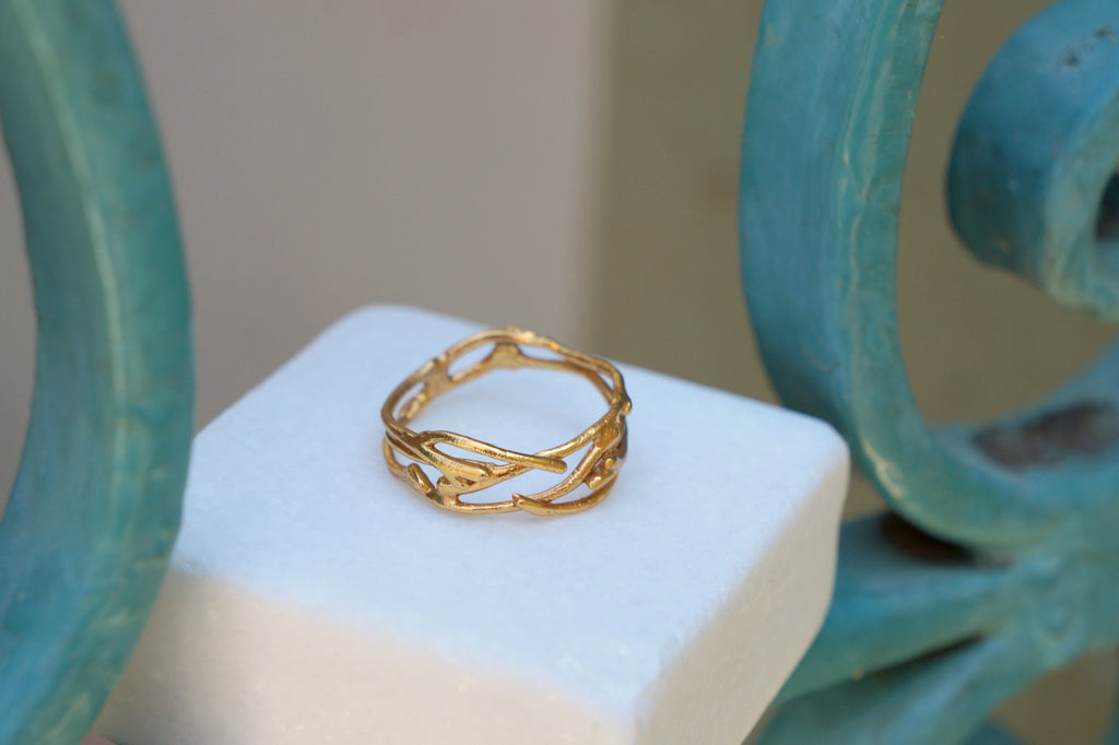 A gold ring with a unique, organic design sits on a white surface, with a blue metal railing visible in the background.