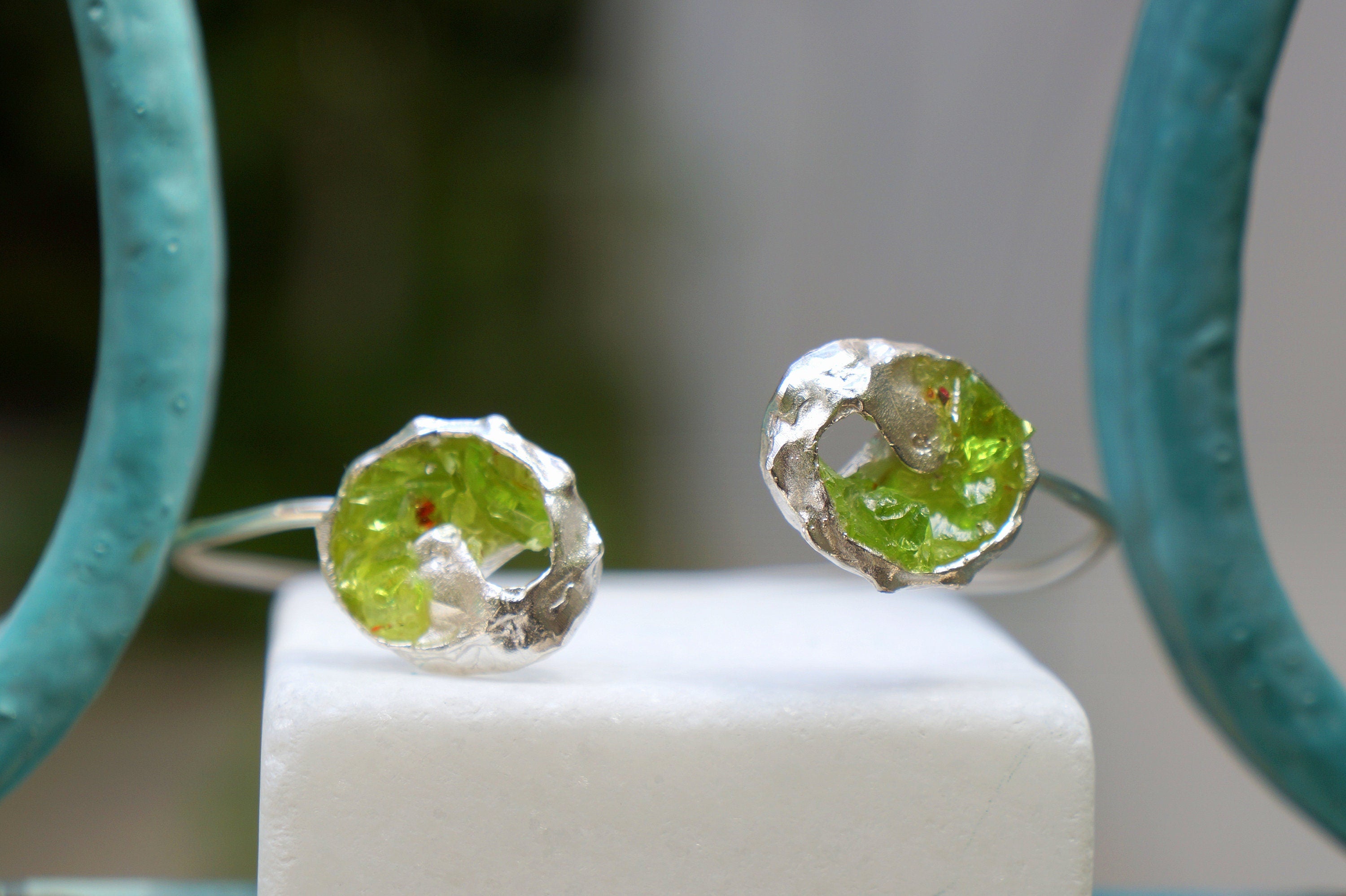 two silver rings with green gemstones, one on each side of a white pedestal.