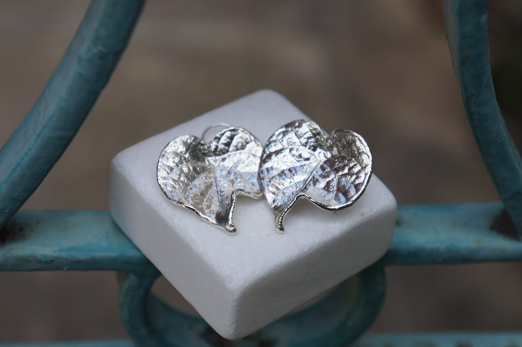 A pair of silver leaf-shaped earrings resting on a white square surface.