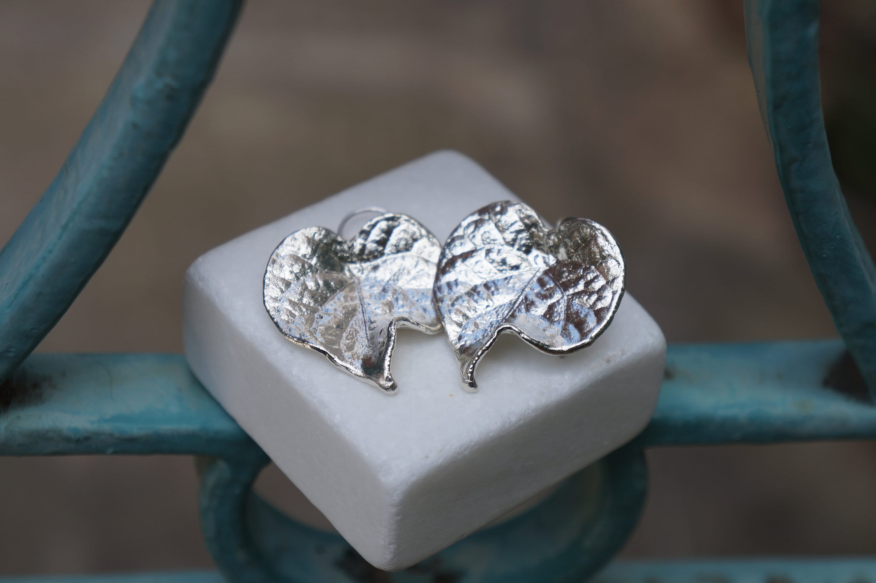 A pair of silver leaf-shaped earrings resting on a white square surface.