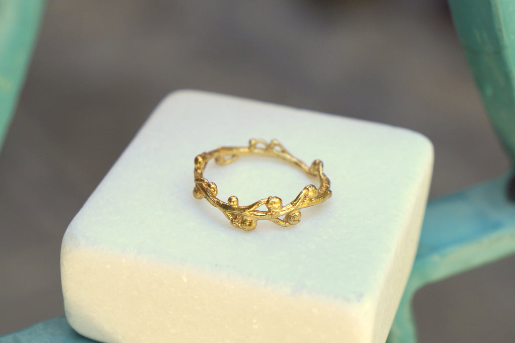 A gold ring with a leaf-like design sits on a white square surface.