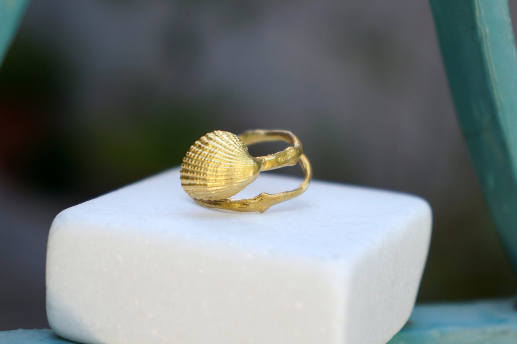 A gold ring with a shell-shaped design sits on a white surface.