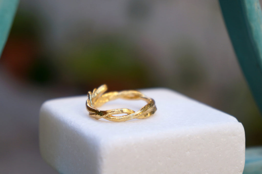 A gold ring with a leaf-like design sits on a white pedestal. Gold Unique twig ring