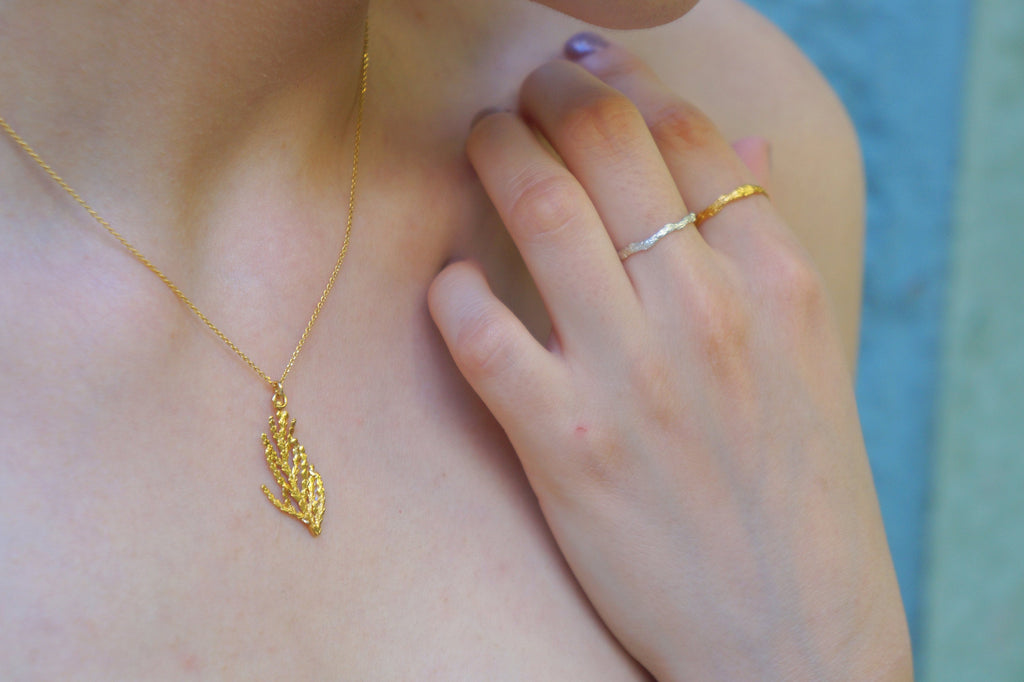 A close-up of a person's hand wearing a gold necklace and two rings, with a blurred background.
