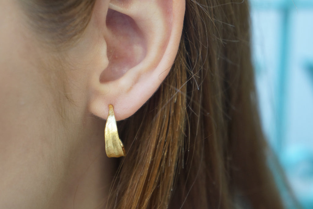 A close-up view of a person's ear adorned with a gold hoop earring.