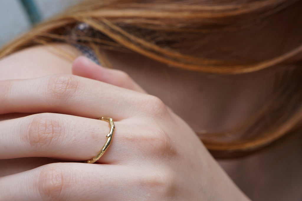 A close-up view of a person's hand wearing a gold ring, with their hair visible in the background.