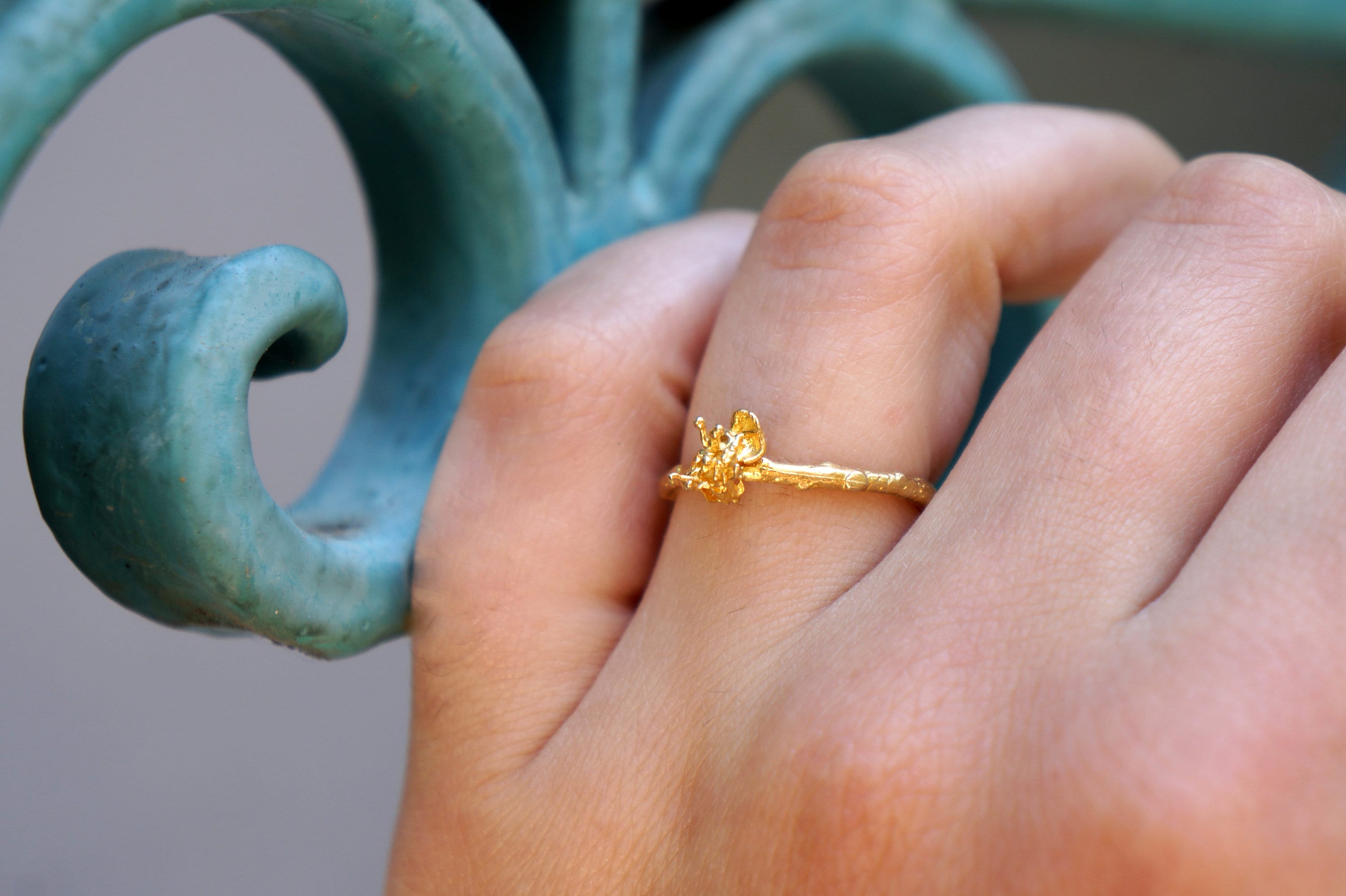 A close-up of a person's hand wearing a gold ring with a small flower design.