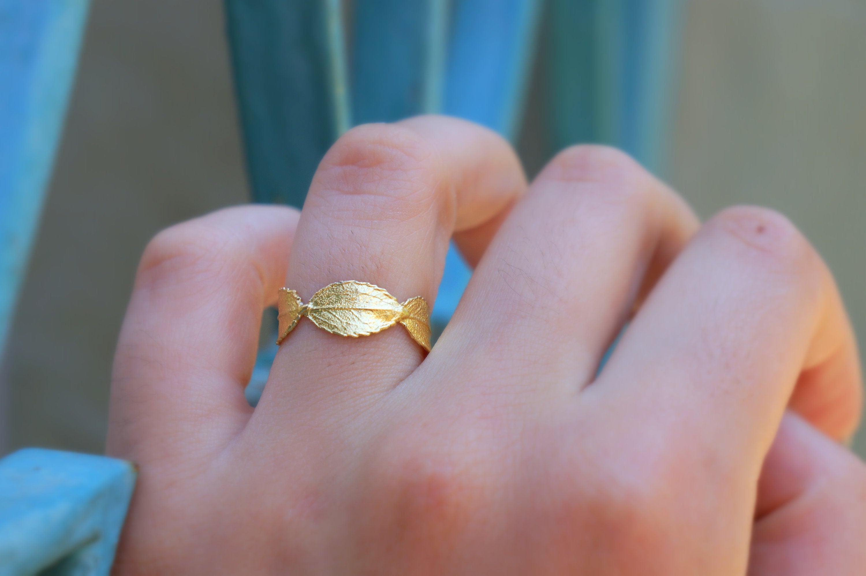 A close-up of a person's hand wearing a gold leaf-shaped ring.