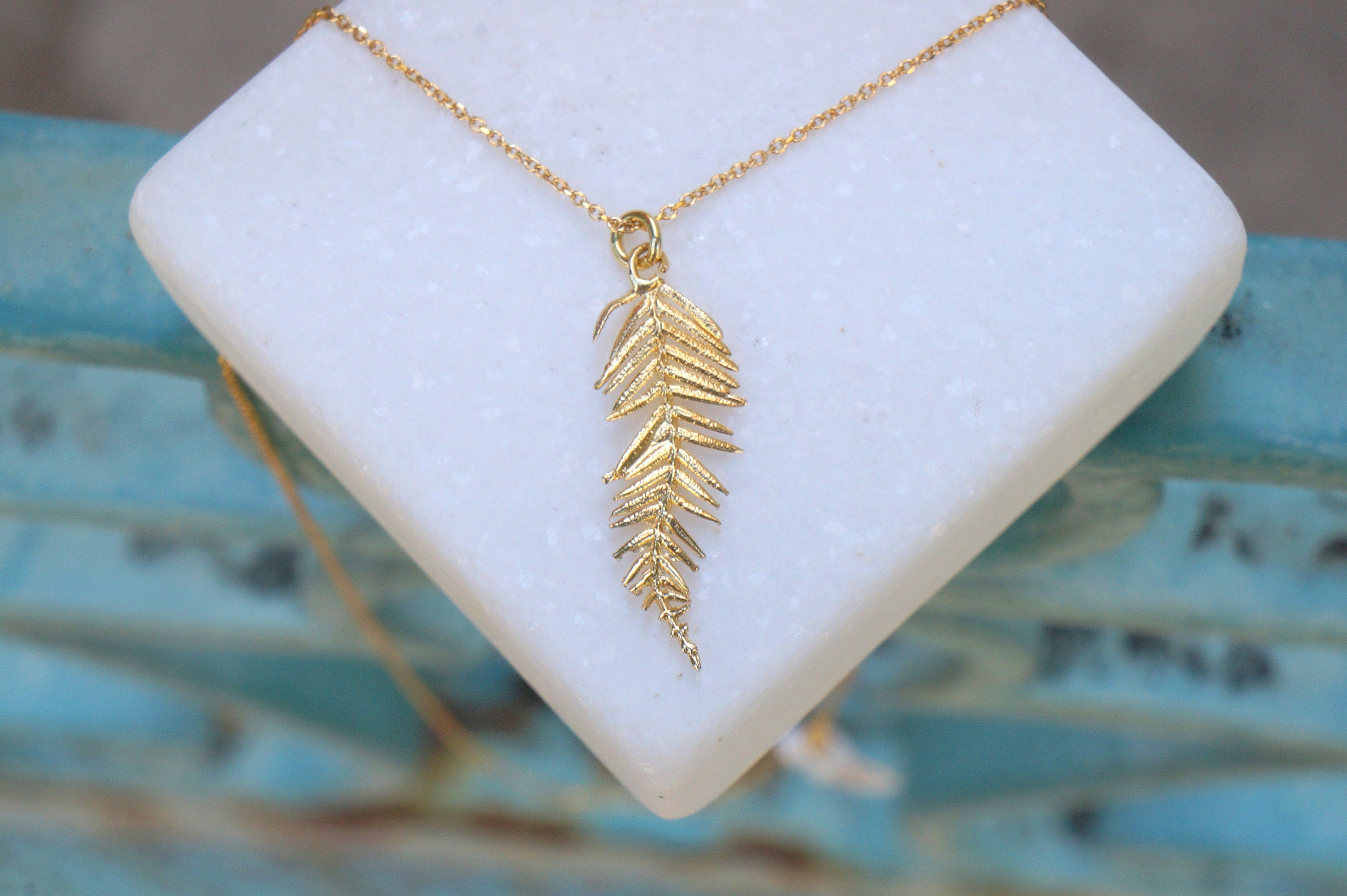 A gold-colored necklace with a pendant featuring a leaf design is displayed on a white marble surface.