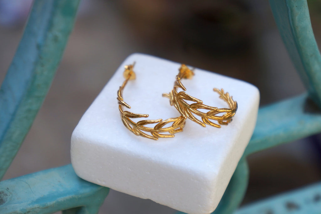 A pair of gold earrings with leaf-like designs, resting on a white surface.