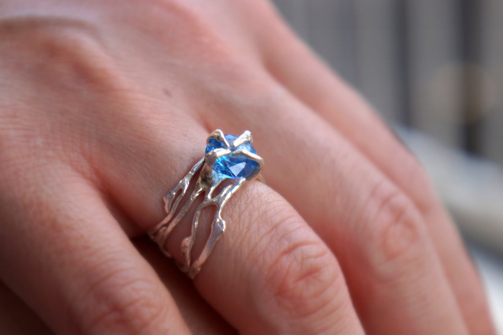 A close-up of a person's hand wearing a silver ring with a blue gemstone.