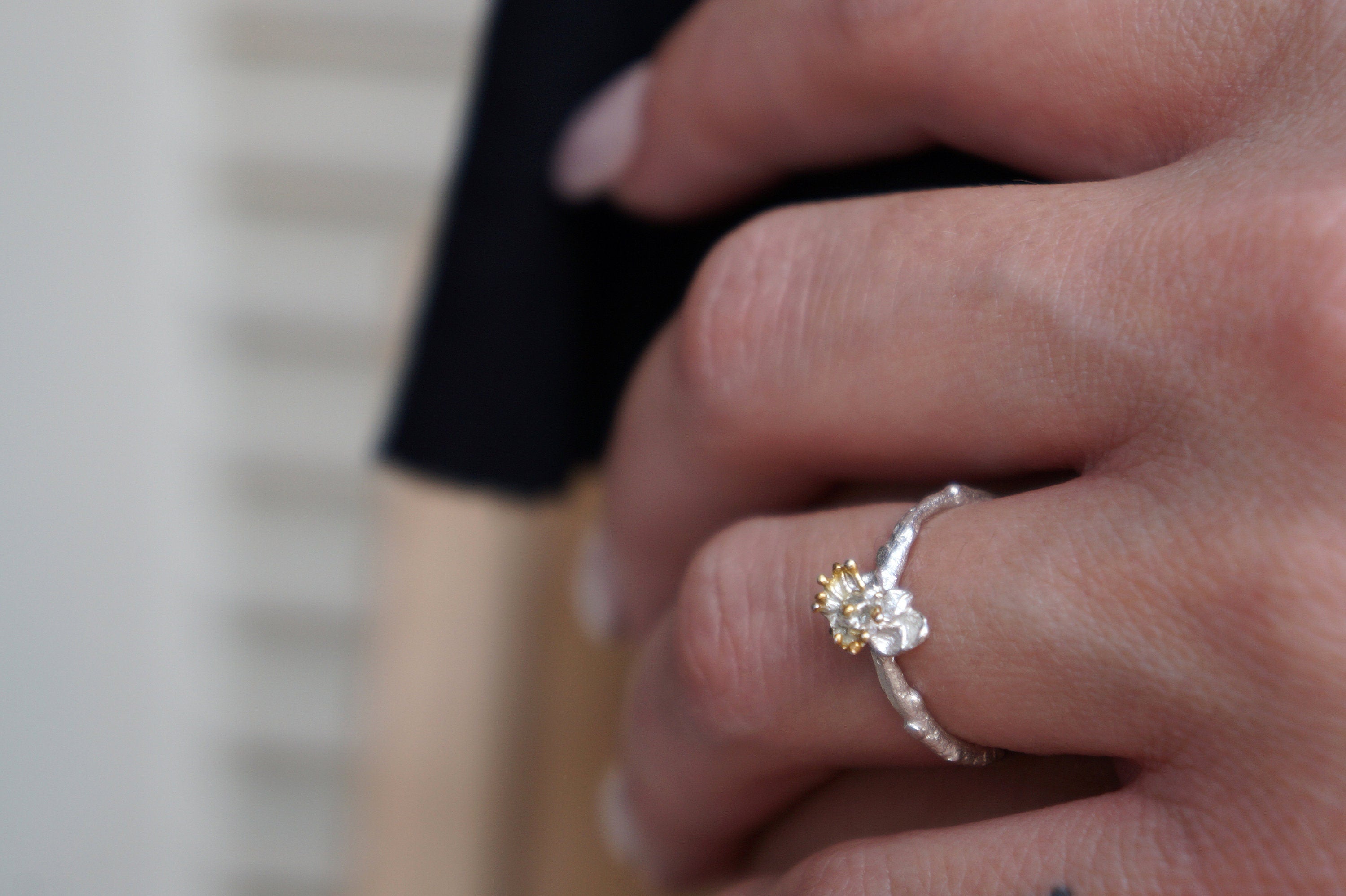 A close-up of a person's hand wearing a silver ring with a small yellow flower on it.