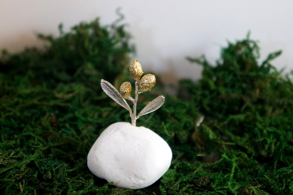 A small white stone with a gold leaf-like decoration sits on a bed of green moss.