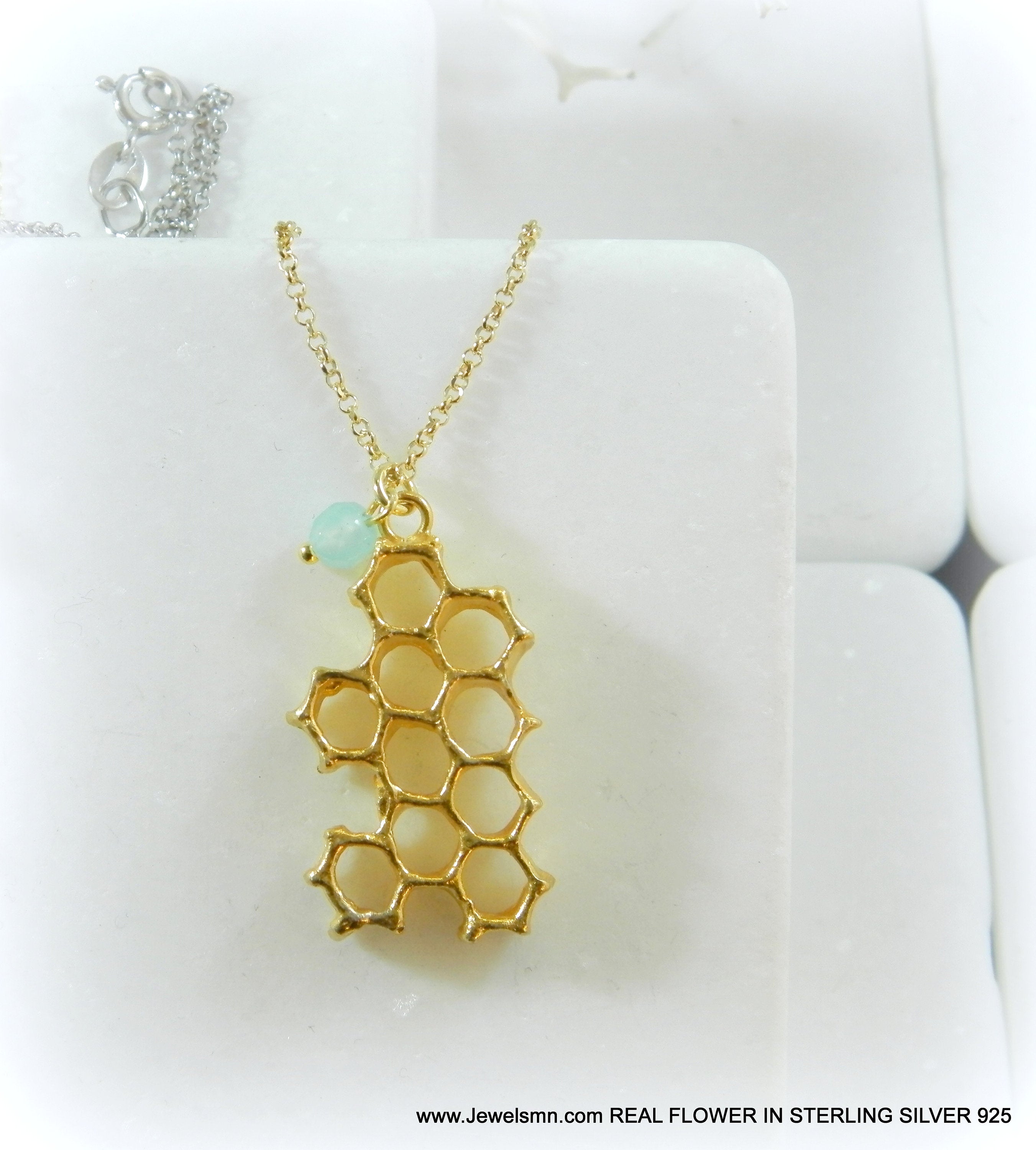 A gold-colored pendant necklace with a honeycomb-shaped pendant is displayed against a white background.