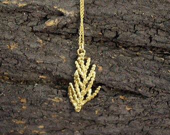 A delicate gold leaf pendant is suspended from a chain, resting on a rough, textured surface.