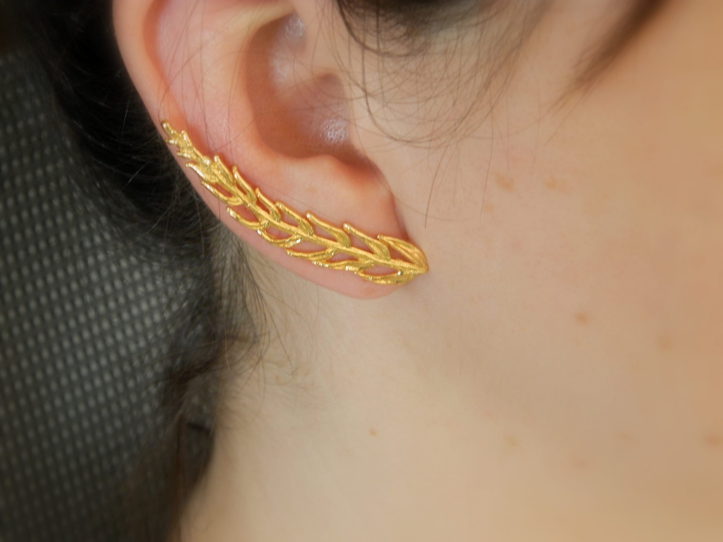 A close-up view of a person's ear adorned with a gold leaf earring.