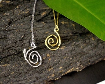 Two spiral pendants in silver and gold colors are hanging from a chain, suspended against a dark brown background with a green leaf.