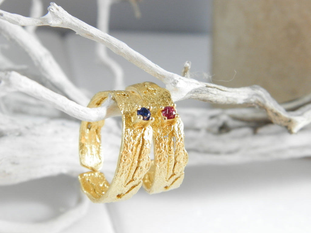 Two gold rings with gemstones are hanging from a white branch.