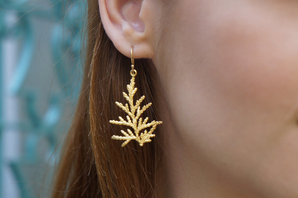 A close-up view of a person's ear wearing a gold earring shaped like a leaf or branch.