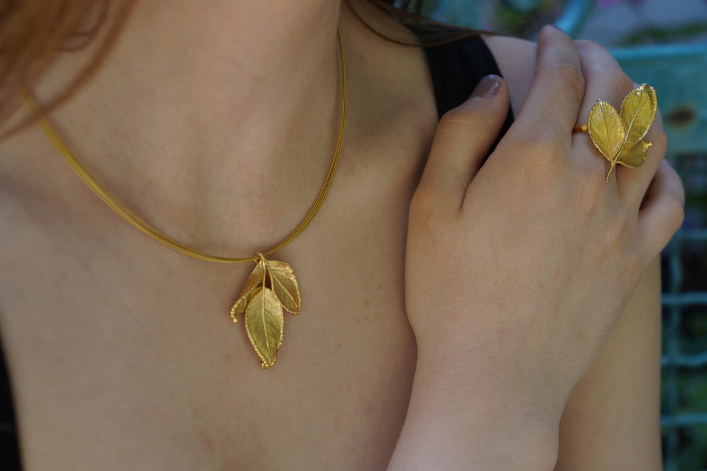 A close-up of a woman's neck and chest wearing a gold necklace with a leaf pendant.