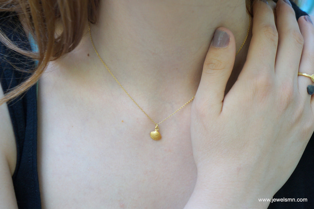 A close-up view of a person's neck and chest area, showing a delicate gold necklace with a small pendant.