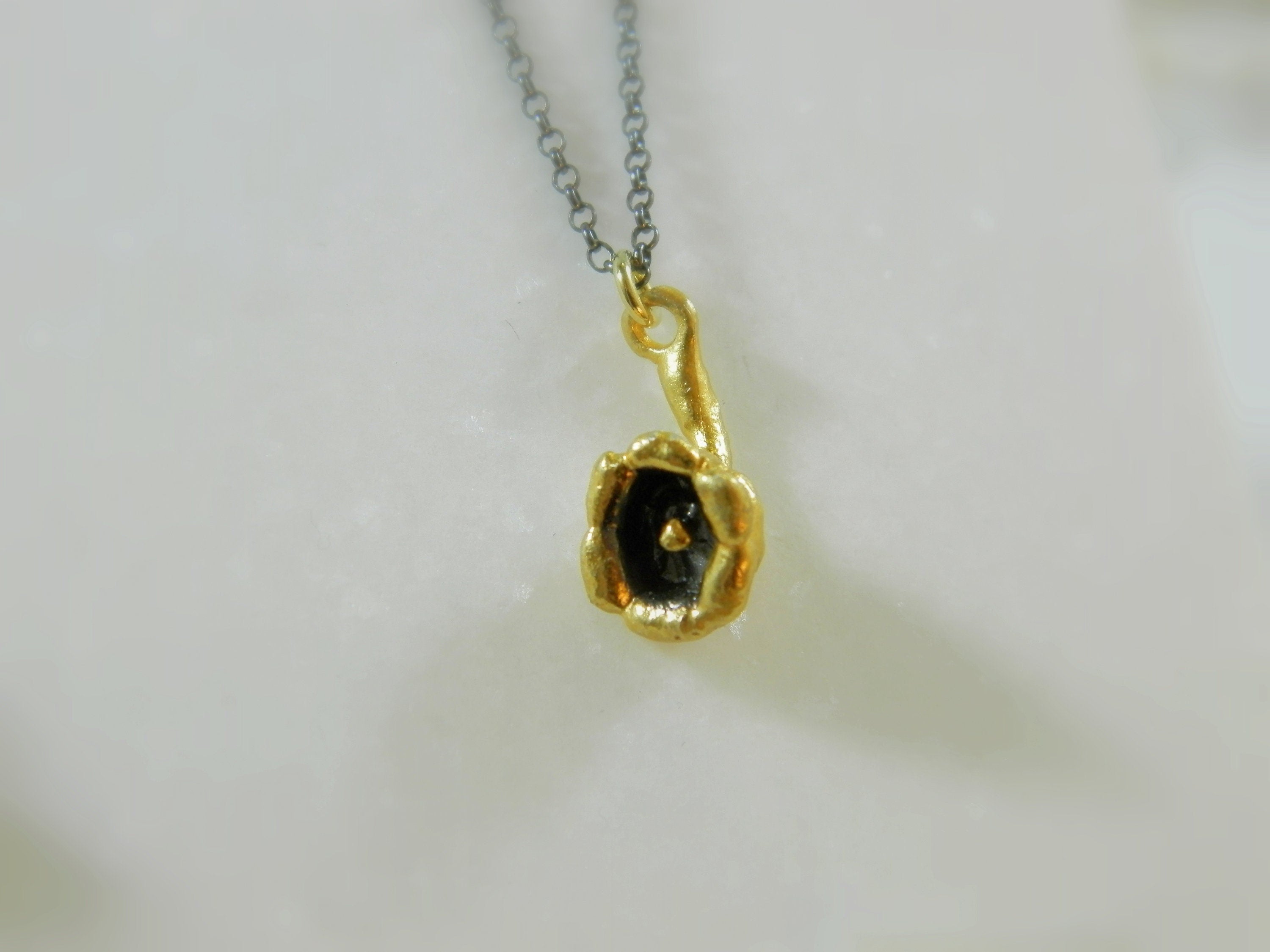 A small, gold-colored pendant with a black center is hanging from a chain against a white background.