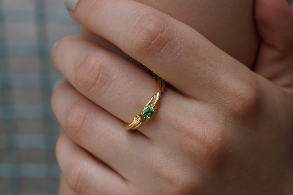 A close-up of a person's hand wearing a gold ring with a green gemstone.