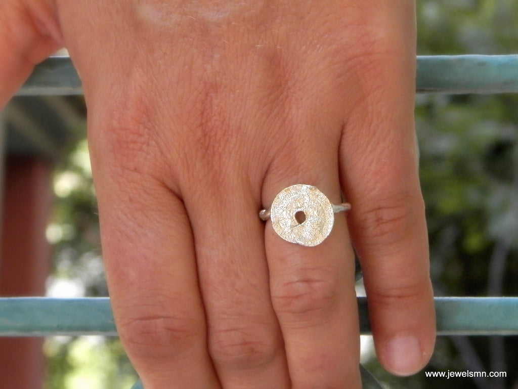 A close-up of a person's hand wearing a silver ring with a circular design.
