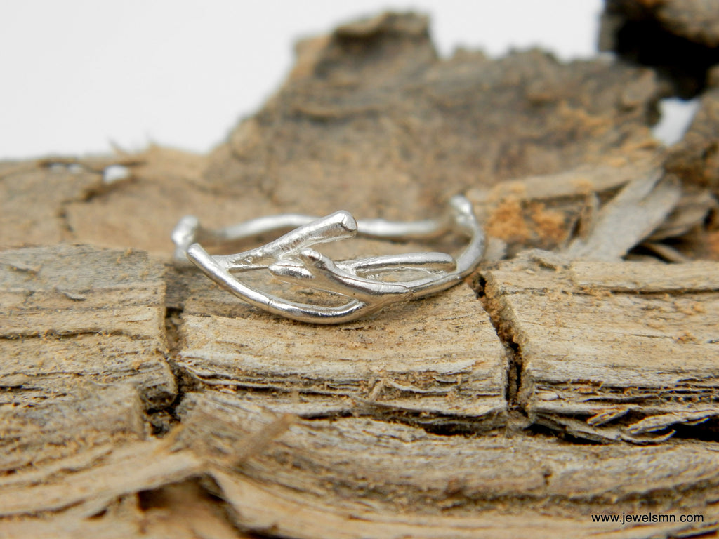 A silver ring with a unique, organic design rests on a piece of weathered, cracked wood.