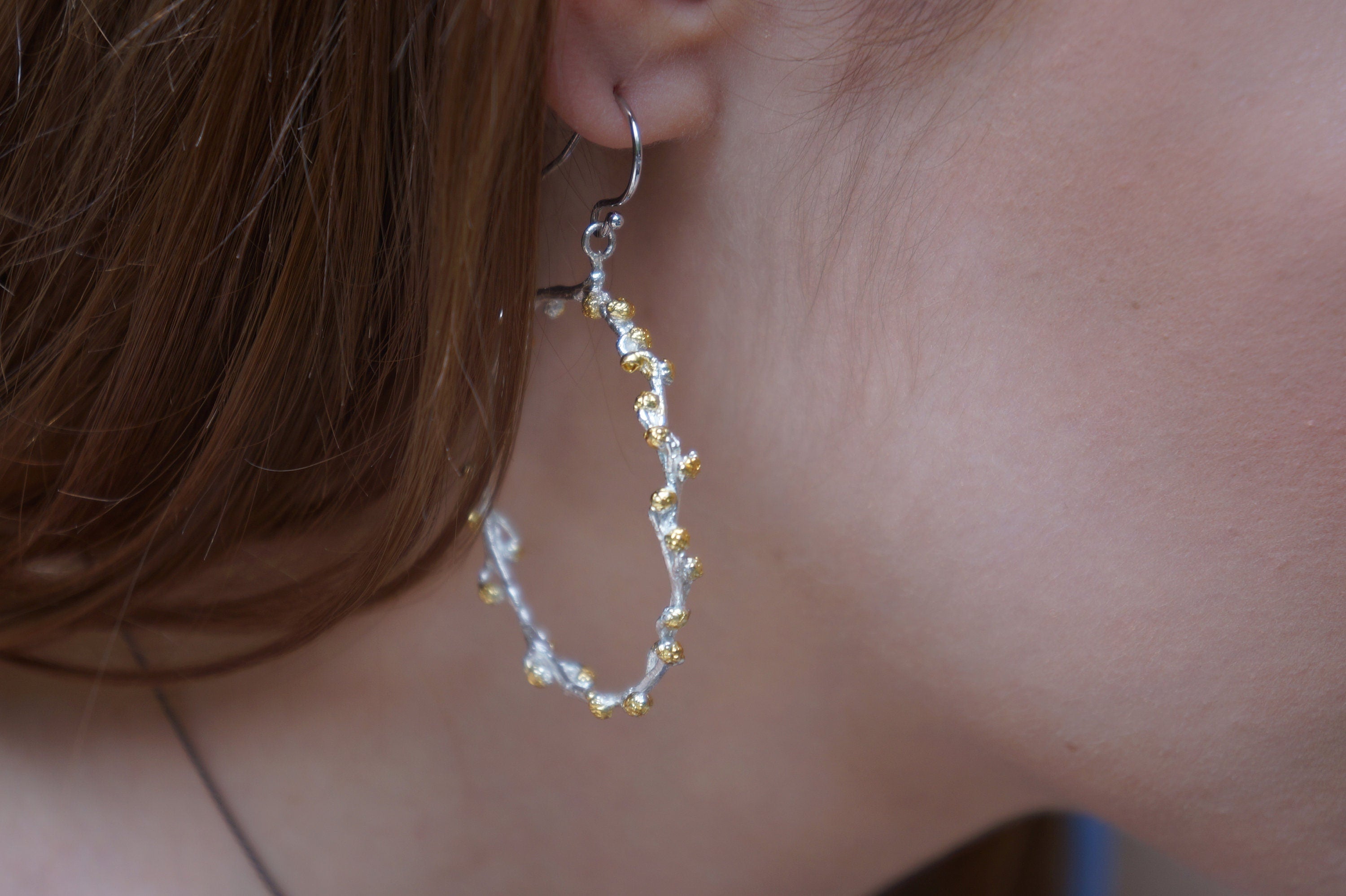 A close-up view of a person's ear wearing a pair of silver earrings with a gold-colored design.