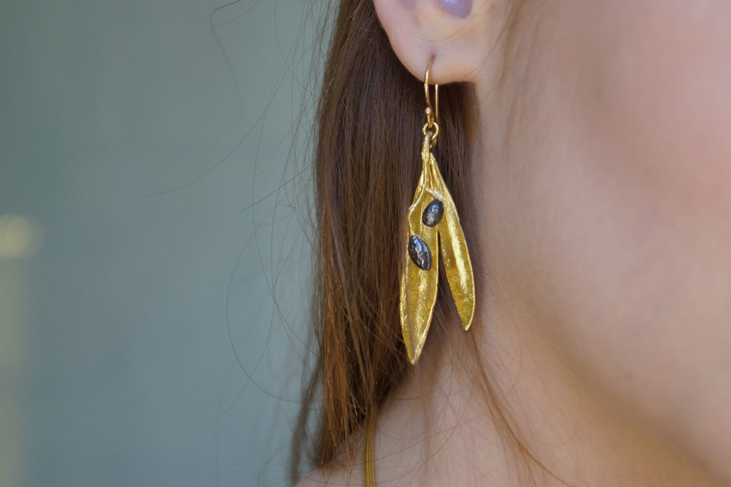 A close-up view of a person's ear wearing a pair of gold earrings with leaf-shaped designs.