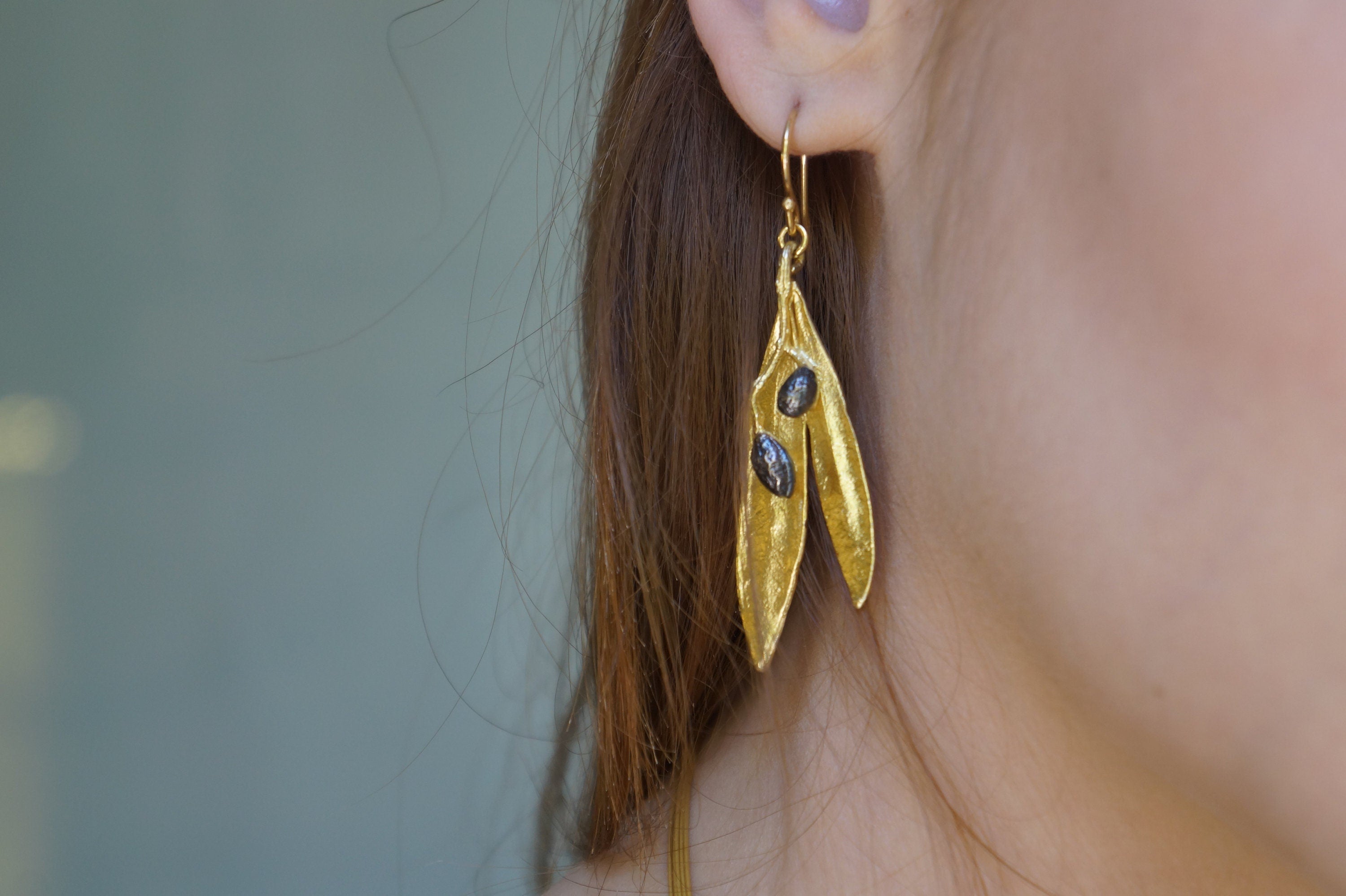 A close-up view of a person's ear wearing a pair of gold earrings with leaf-shaped designs.