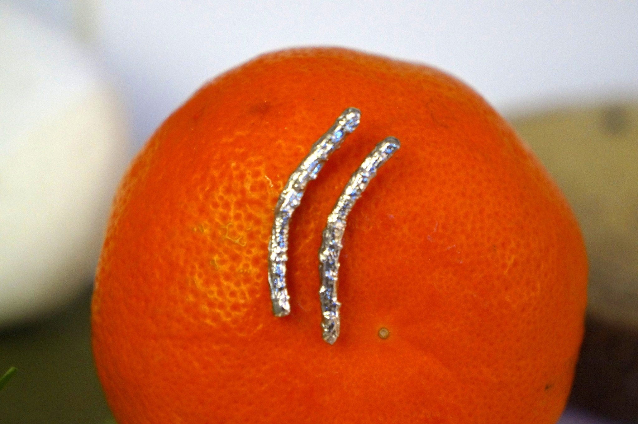 A close-up image of a bright orange fruit with two silver, twisted metal objects resembling a small, metallic plant growing on it.