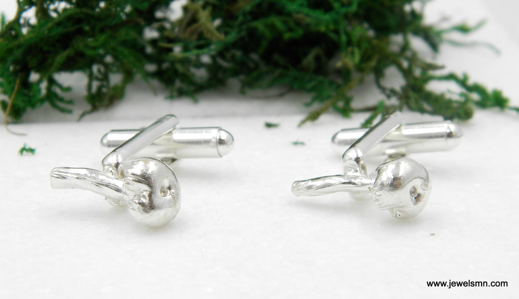 a pair of silver-colored cufflinks placed on a white surface, with a blurred green background.
