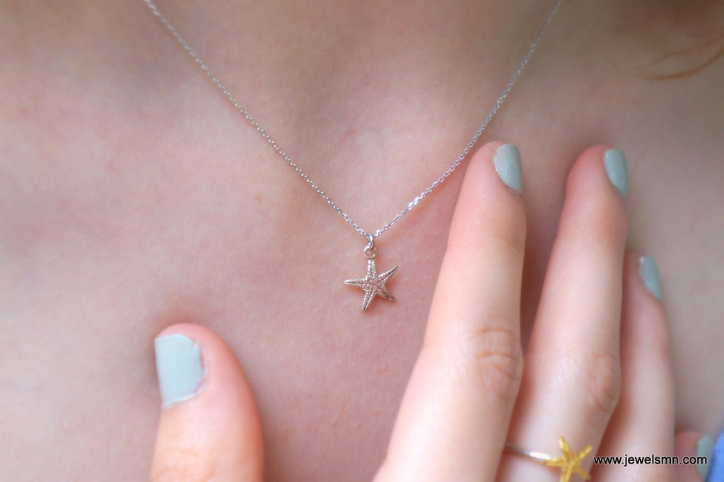 A close-up view of a person's neck and fingers wearing a silver necklace with a star-shaped pendant.