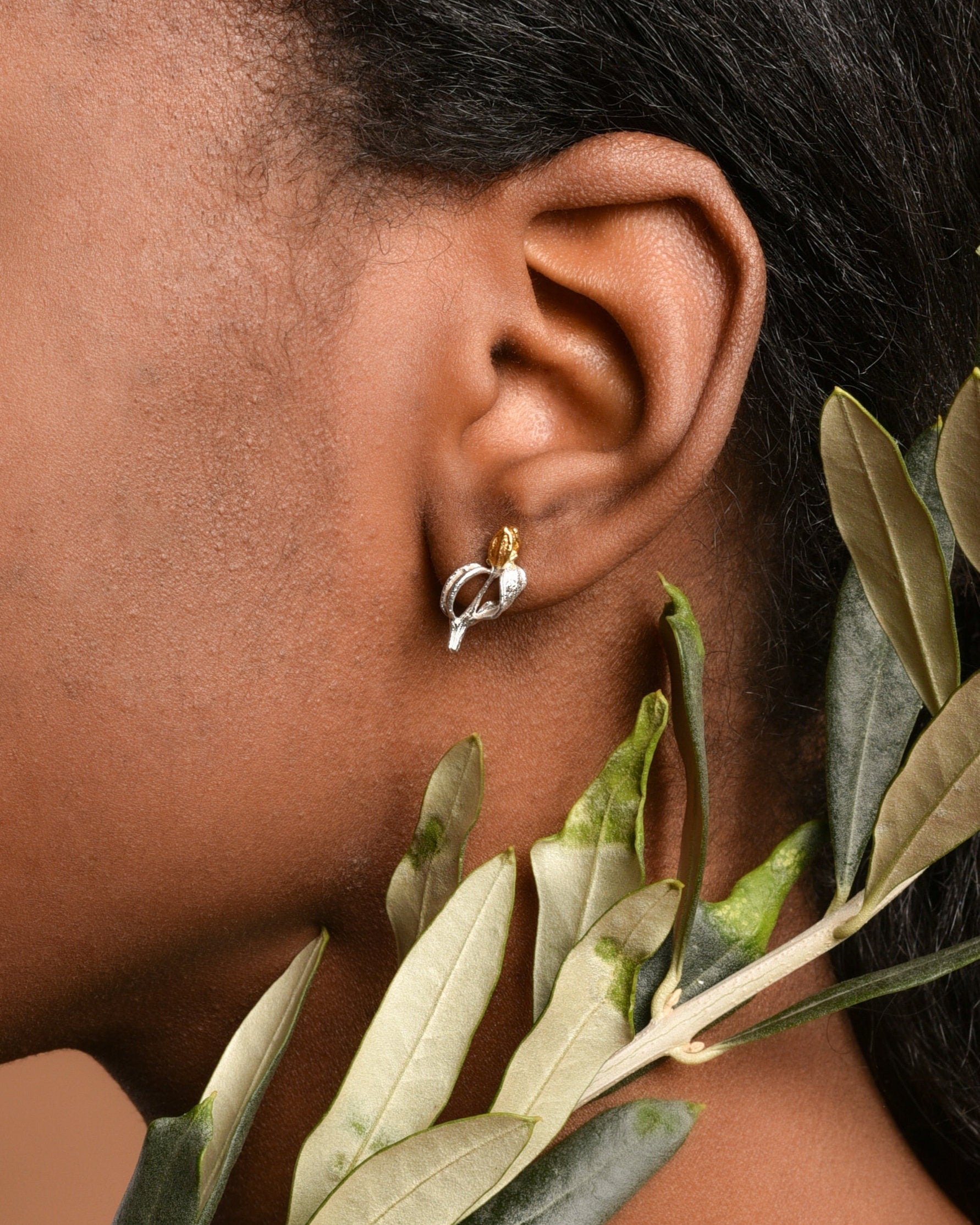 a close-up view of a person's ear adorned with a pair of earrings, surrounded by green leaves.