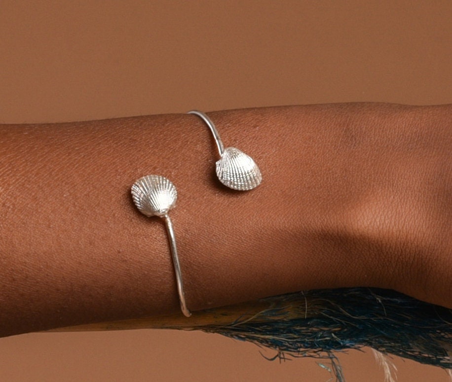 A silver bracelet with two shell-shaped charms is worn on a person's wrist.