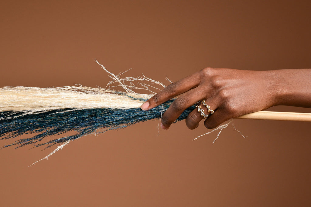 A hand holding a wooden stick with a decorative blue and white fringe attached to it.