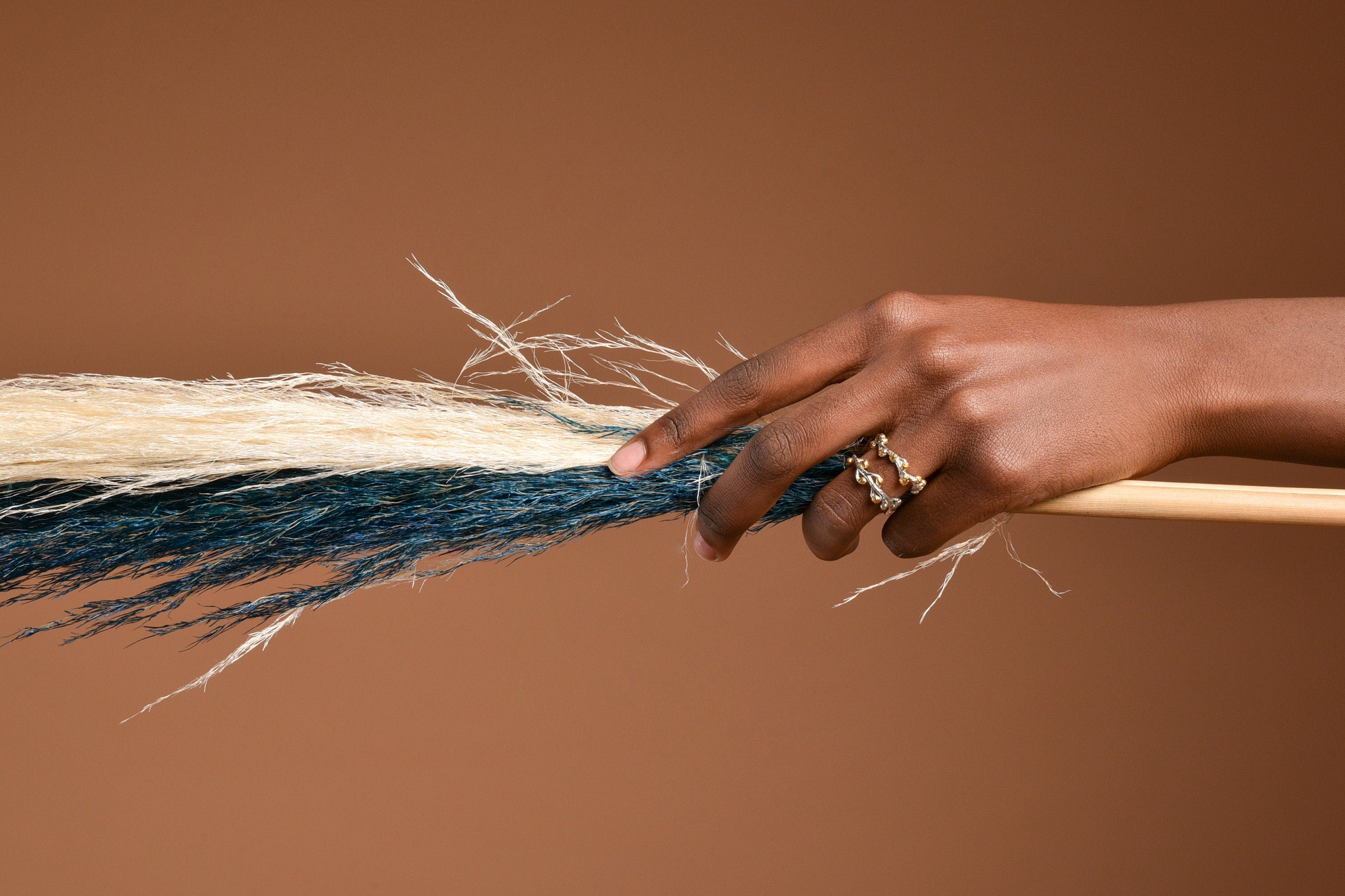 A hand holding a wooden stick with a decorative blue and white fringe attached to it.