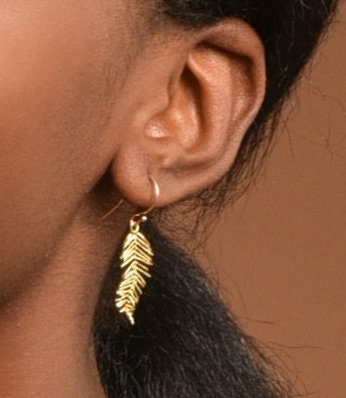 A close-up view of a person's ear adorned with a gold feather earring.