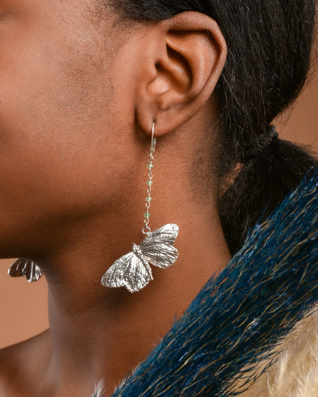 A close-up of a person's ear wearing a pair of silver butterfly earrings with green stones.