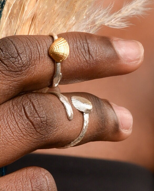 A close-up view of a person's hand wearing two rings, one with a shell design and the other with a leaf design.