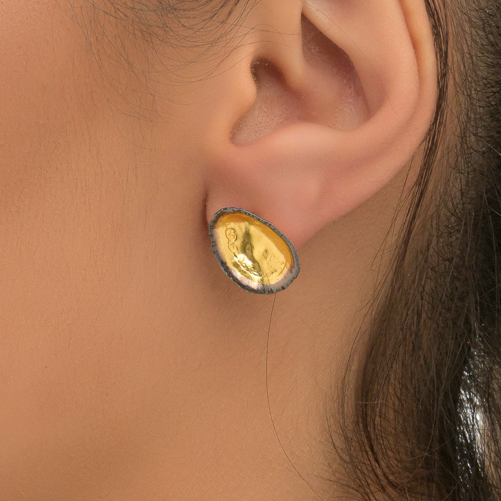 A close-up view of a person's ear wearing a pair of gold earrings with a unique, oval-shaped design.