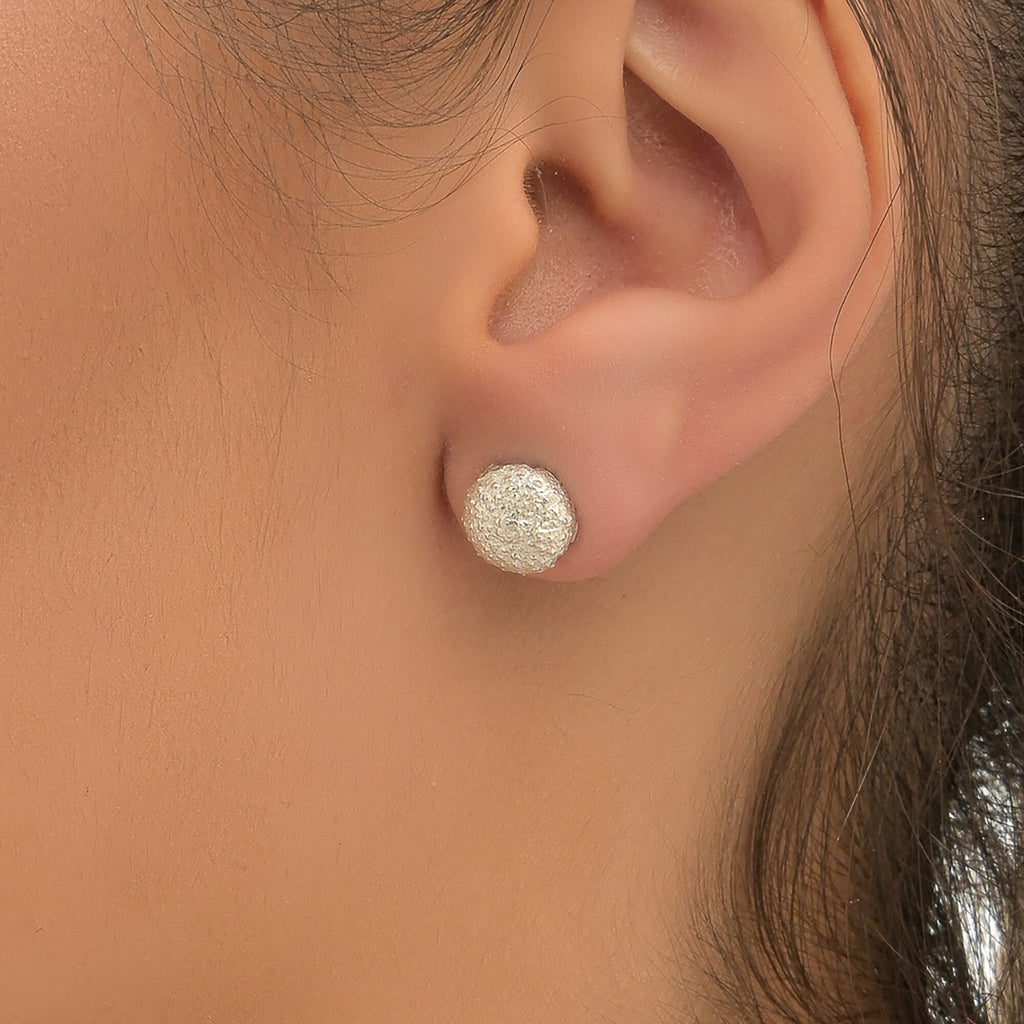 A close-up view of a person's ear, showing a small, round, silver earring with a sparkling, round center.