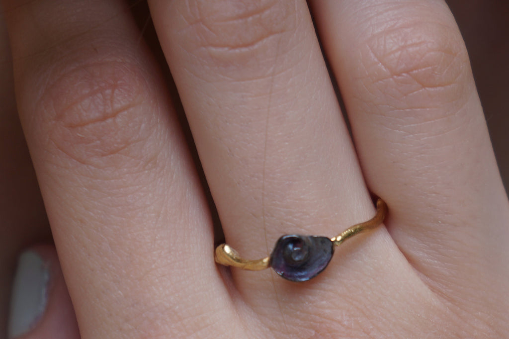 A close-up of a gold ring with a purple gemstone, worn on a person's hand.