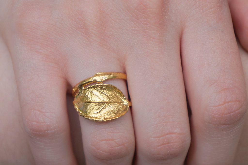 A close-up image of a gold leaf ring on a person's hand.