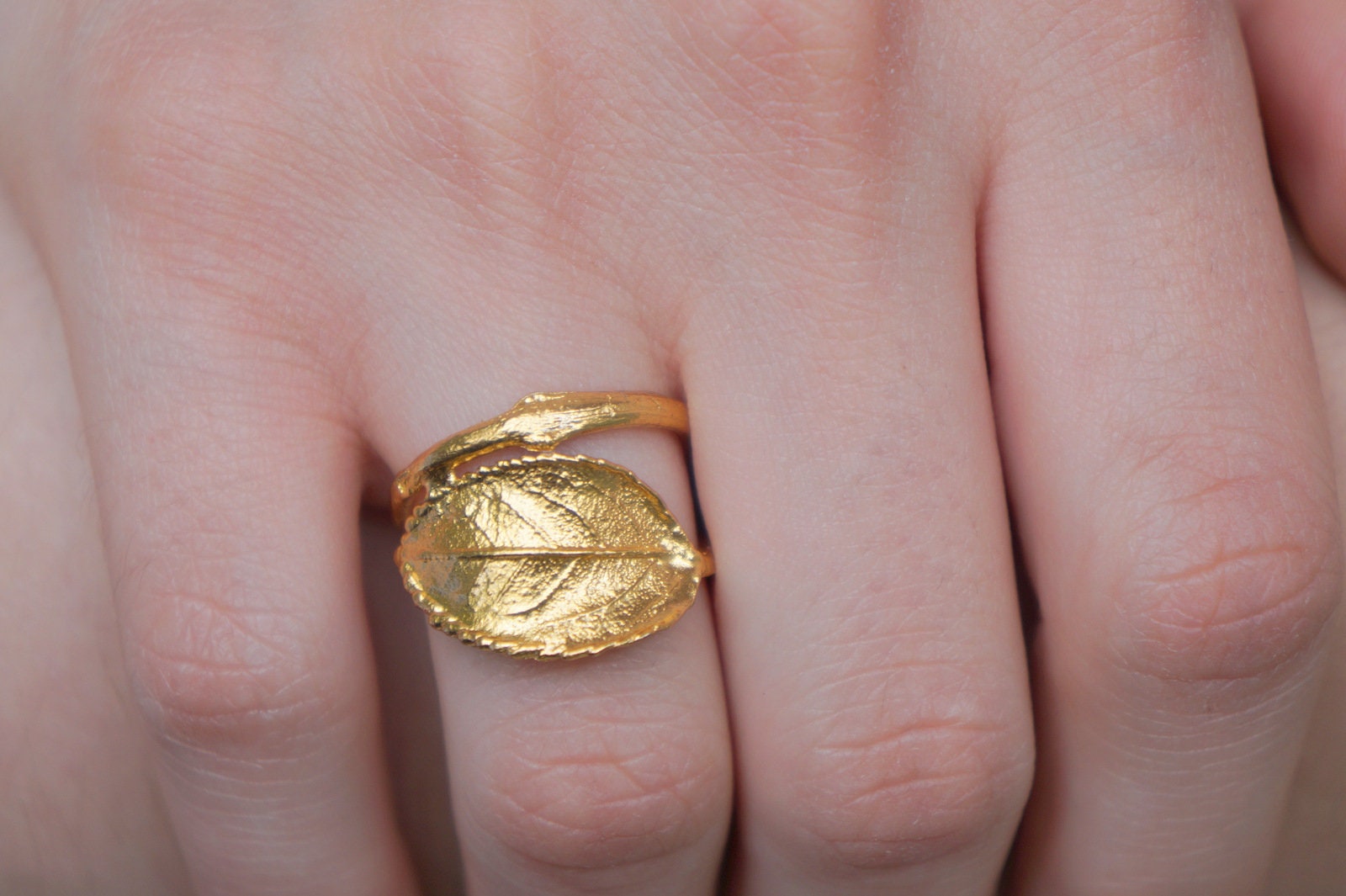 A close-up image of a gold leaf ring on a person's hand.